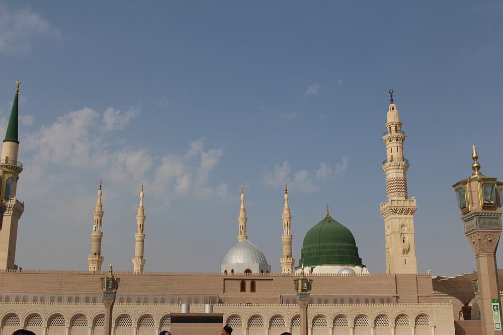 The green dome and minarets of the Prophet's Masjid in Al-Madīnah, against a clear sky.